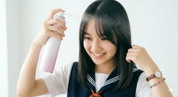 長めの前髪にヘアスプレーをかける女子高校生