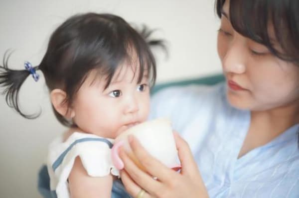 お母さんにストローマグで飲み物を飲ませてもらっている赤ちゃん